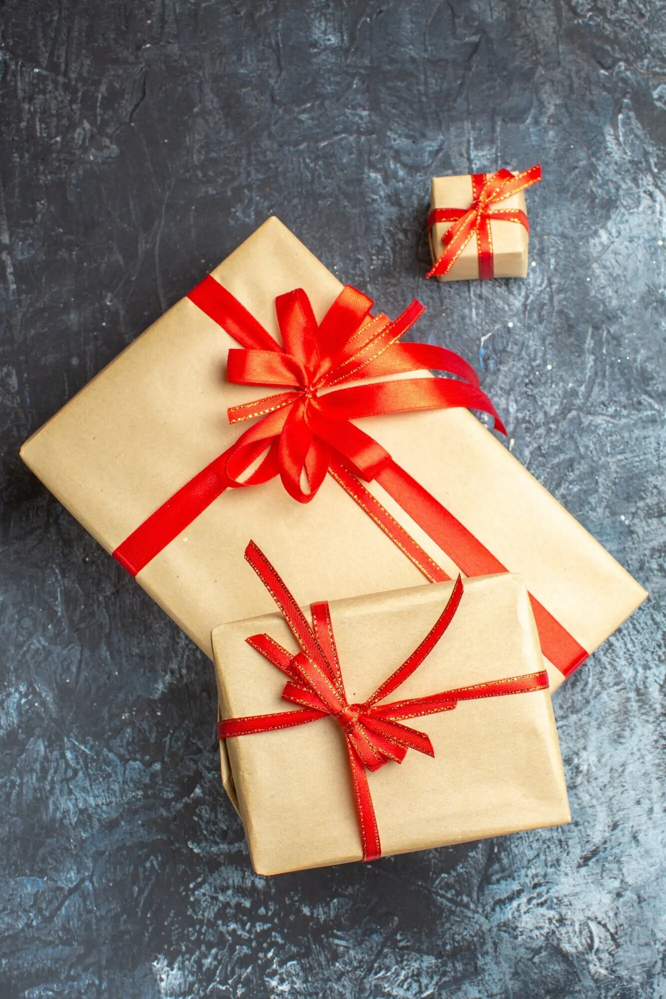 Draufsicht auf Weihnachtsgeschenke, die mit roten Schleifen gebunden sind, vor einem hell-dunklen Hintergrund.