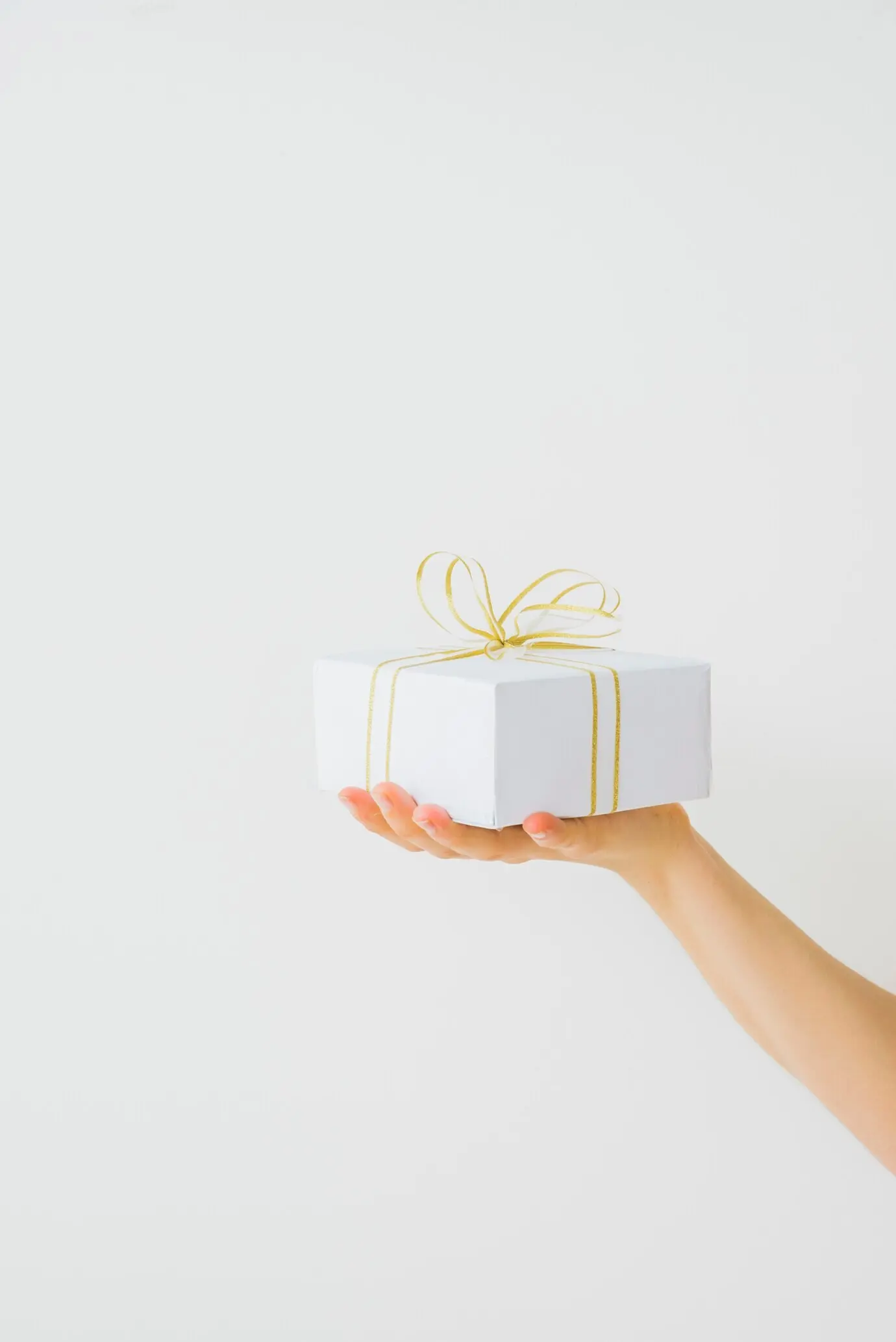 Eine Hand hält ein mit einem Band umwickeltes Geschenk.